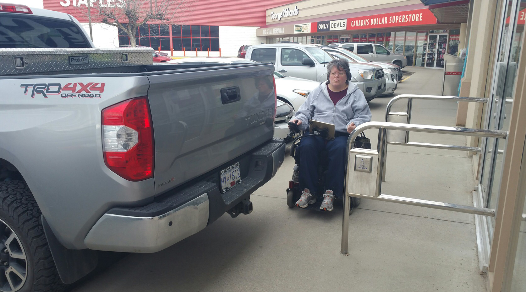 In my wheelchair, on a sidewalk, unable to fit between a railing from a store and the back of an overhanging pick-up truck